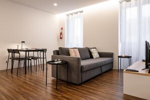 A modern living room with a grey sofa, a small round table, a desk with a computer, and a chair. - Cozy Figueira Apartment (Figueira da Foz)