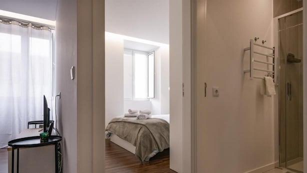 A modern hotel room with a bed, a desk, a shower, and a view of the outdoors. - Cozy Figueira Apartment (Figueira da Foz)
