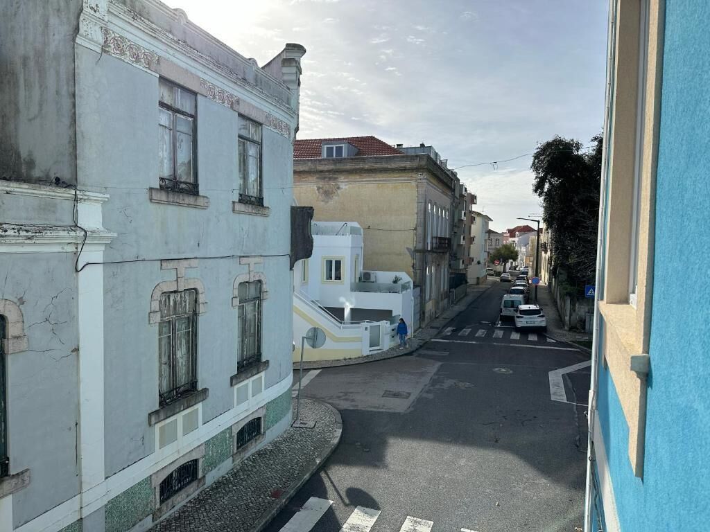 Una calle estrecha flanqueada por edificios, con un paso de peatones y coches aparcados.