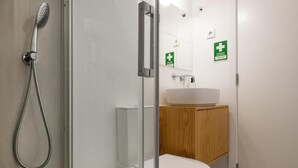 A modern bathroom with a glass shower enclosure, a white toilet, and a wooden cabinet. - Cozy Figueira Apartment (Figueira da Foz)