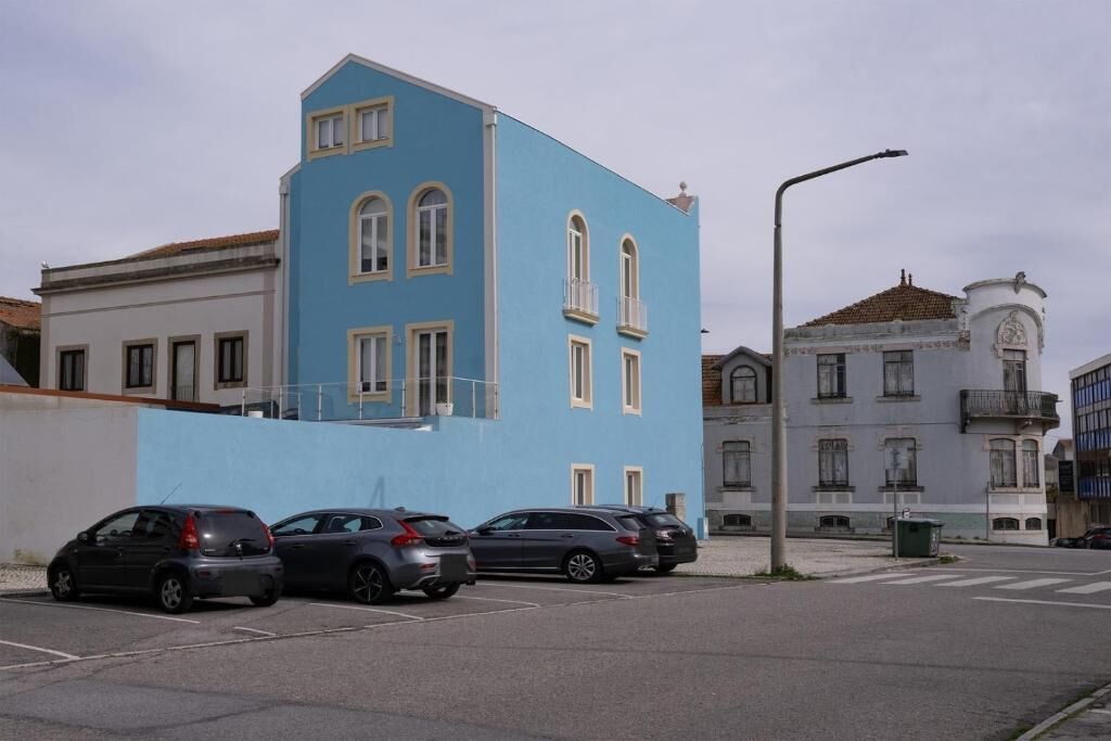 A street view with a blue building, parked cars, and a streetlight.