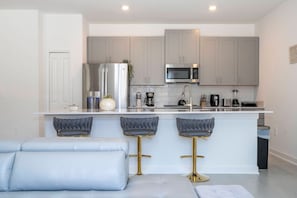 A modern kitchen with grey cabinets, a stainless steel refrigerator, a microwave, and a bar area with stools. - 4BR Home at Storey Lake w/ Private Pool (Kissimmee)