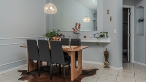 Uma área de refeições com mesa de madeira, cadeiras pretas, tapete de couro bovino e iluminação pendente.