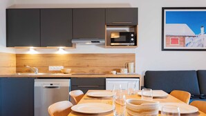 A modern kitchen with dark cabinets, a microwave, and a dining area set for four with plates, glasses, and cutlery. - Résidence Eden - Living Stone (Vars)