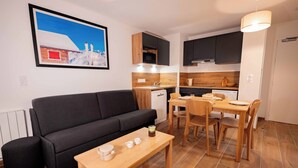 A compact living space with a sofa, a dining table, and a kitchen area. - Résidence Eden - Living Stone (Vars)