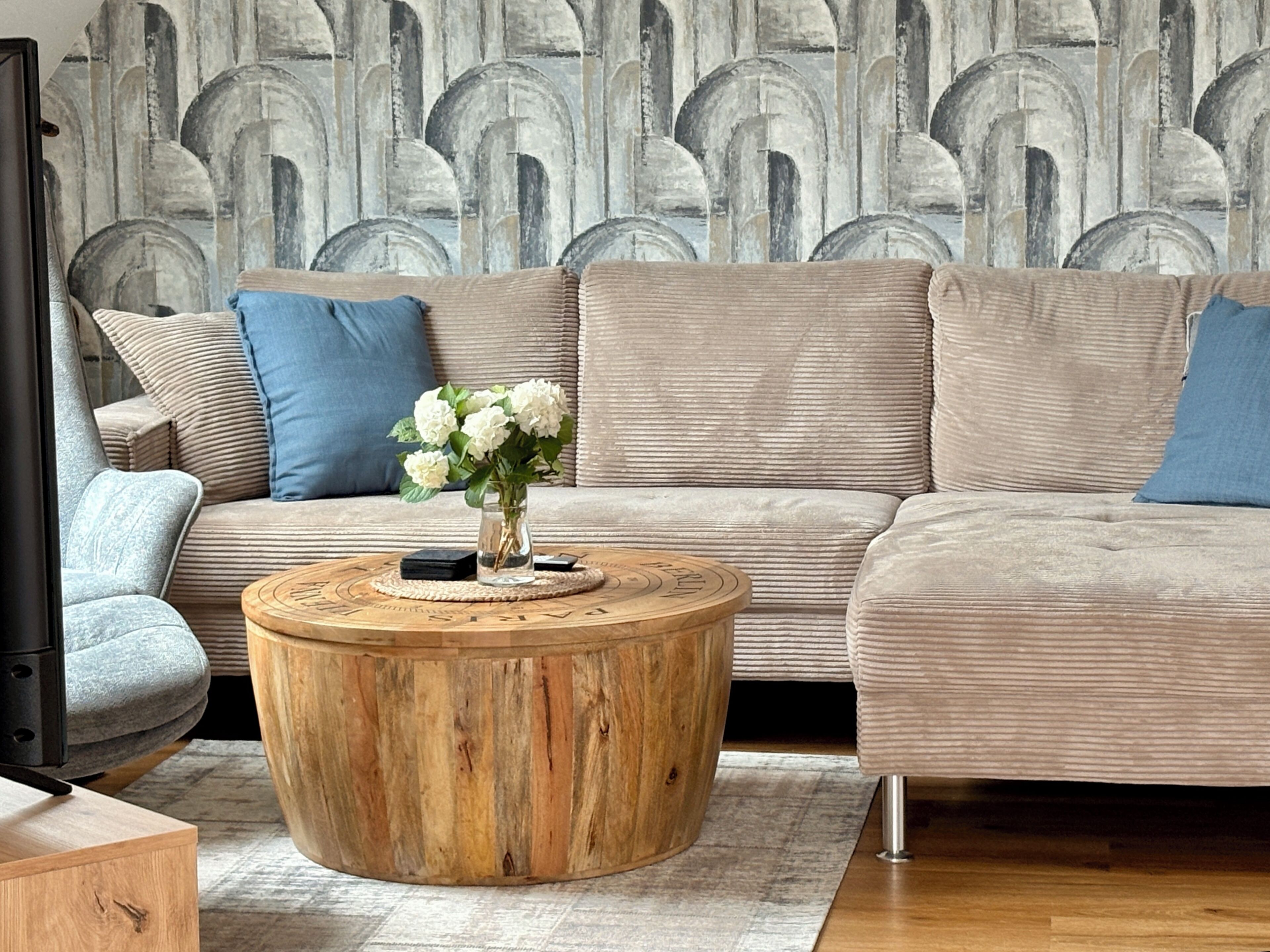 A modern living room with a sectional sofa, a round wooden coffee table, and a vase of white flowers.
