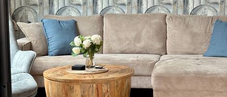 A modern living room with a sectional sofa, a round wooden coffee table, and a vase of white flowers.