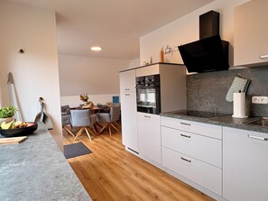 A modern kitchen with white cabinets, a built-in oven, and a black range hood. - 4 room apartment close to the beach Apartment with large 30m² balcony (Büsum)