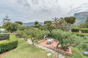 Un patio con mobiliario exterior, rodeado de exuberante vegetación y un paisaje montañoso.