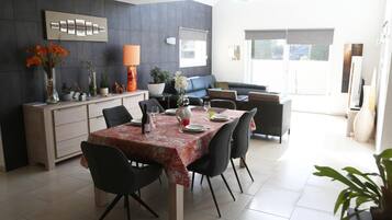 Un espace repas moderne avec une table dressée pour quatre personnes, un canapé et un coin cuisine équipé de placards et d’un réfrigérateur.