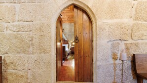A stone wall with a wooden door leading to a room with a bed and a lamp. - Princess Suite at the Castle of Portugraal (Vilela)