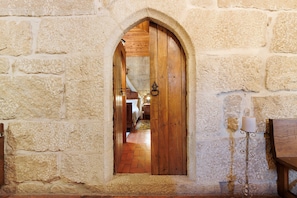 Un muro de piedra con una puerta de madera que da a una habitación con una cama y una lámpara.