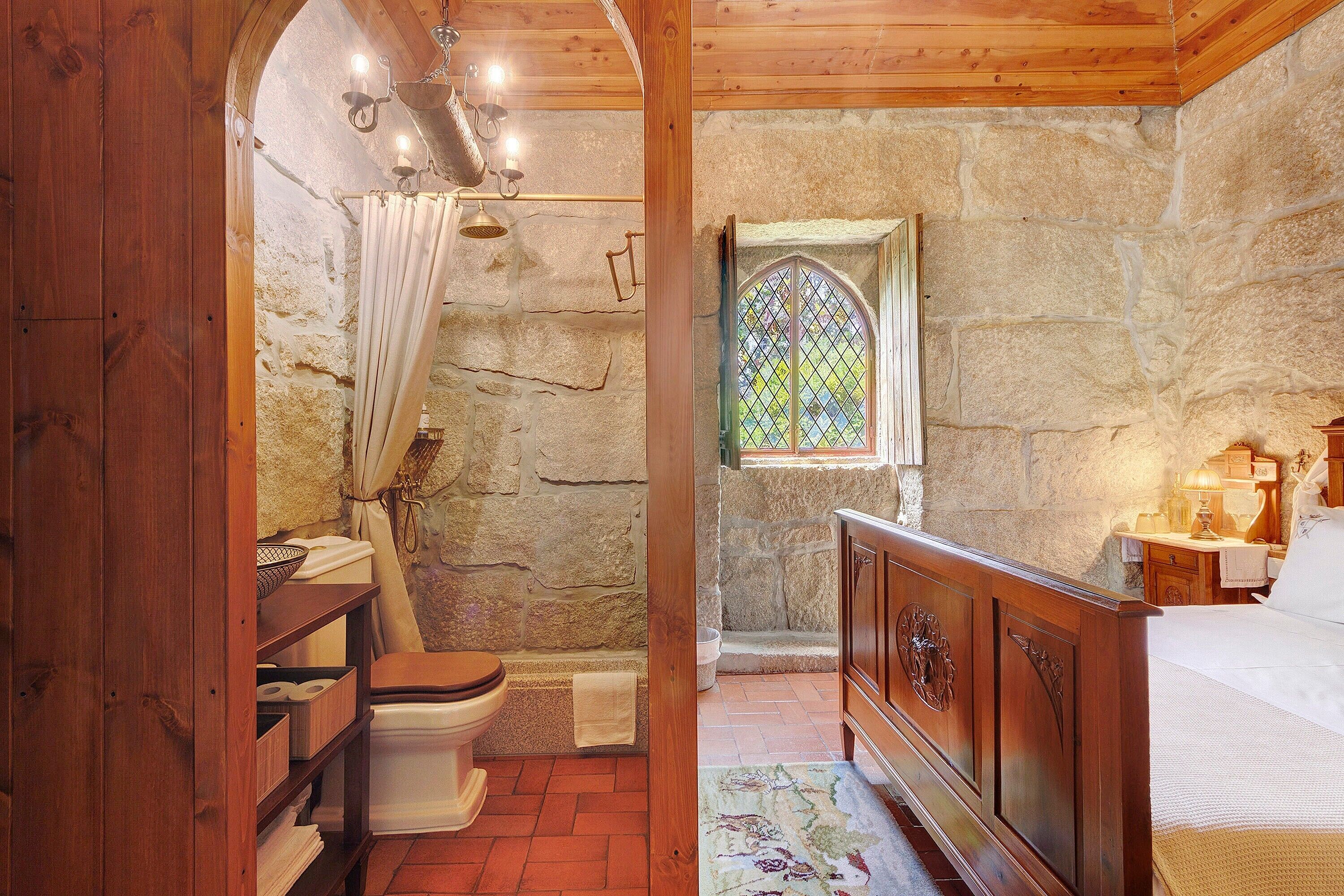 Une salle de bain rustique avec un banc en bois, un mur en pierre, une porte en bois et une fenêtre avec des vitraux.