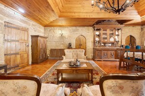 A traditional interior with wooden ceilings, stone walls, a central sofa, a coffee table, and a dining area with chairs and a table. - Princess Suite at the Castle of Portugraal (Vilela)