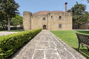 Un bâtiment en pierre avec une entrée centrale, un chemin pavé menant à l’entrée et un banc situé sur la droite.