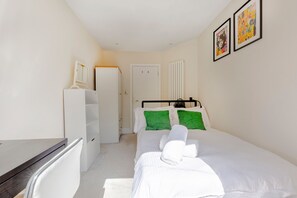 Ein Schlafzimmer mit Bett, Schreibtisch, Stuhl, Kleiderschrank und zwei gerahmten Bildern an der Wand.