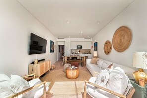 A modern living room with a flat-screen TV, a sofa, a dining area, and a kitchen in the background. - Casa da Saudade in Tavira (Tavira)