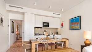 A modern kitchen with white cabinets, a microwave, and a dining area with a wooden table and chairs. - Casa da Saudade in Tavira (Tavira)