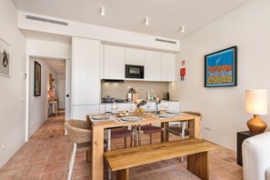 A modern kitchen with white cabinets, a microwave, and a dining area with a wooden table and chairs. - Casa da Saudade in Tavira (Tavira)