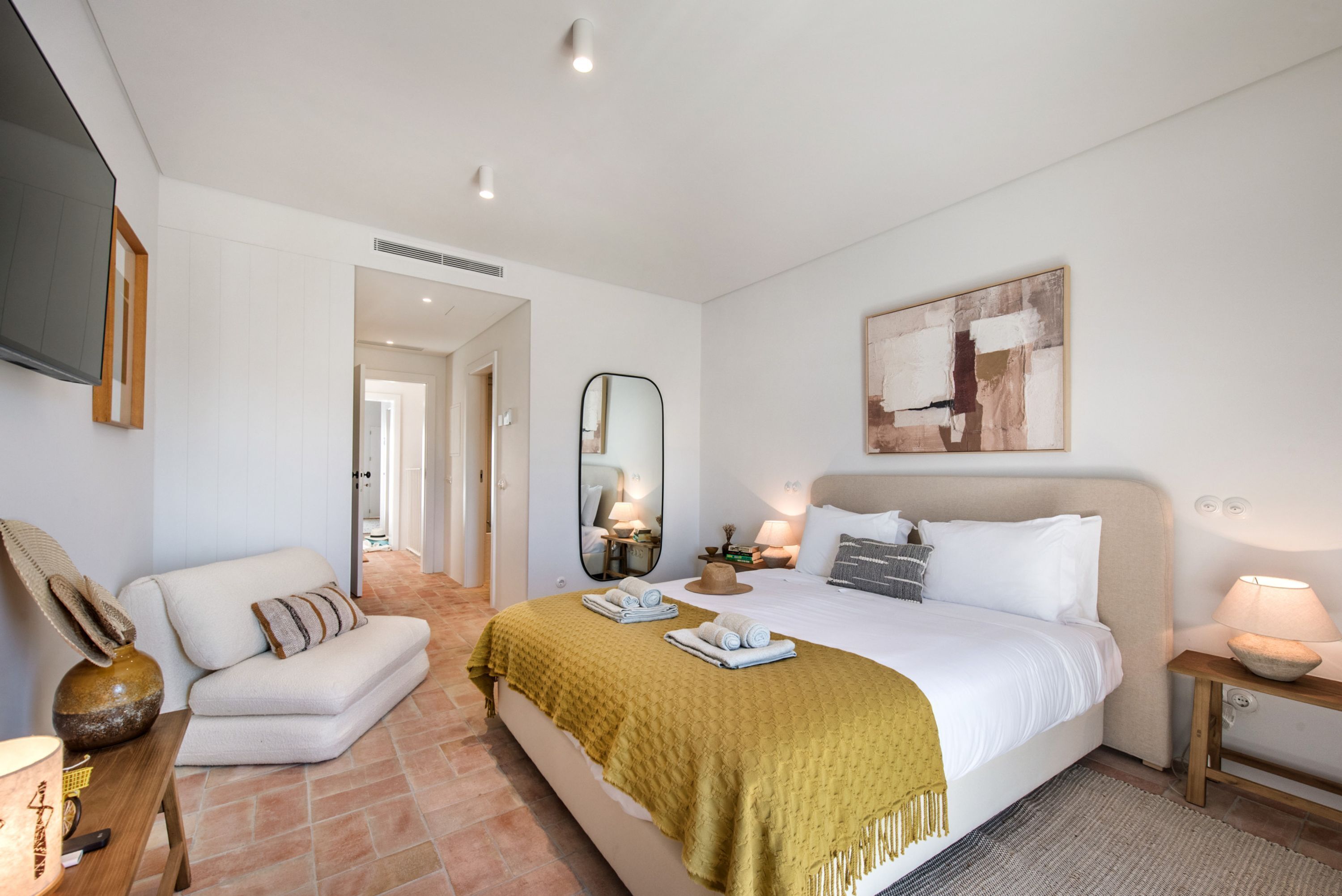 Um quarto com cama, sofá, espelho, abajur e um quadro na parede.