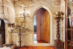 Una habitació amb parets de pedra, una porta de fusta, un candelabrum i un suport decoratiu.