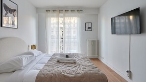 Ein Schlafzimmer mit einem Bett, einem Fernseher, einer Heizung und einem Fenster mit Vorhängen.