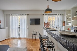 Eine moderne Küche mit schwarzem Arbeitsplatz, zwei Barhocker, einer hängenden Pendelleuchte und Blick durch das Fenster.
