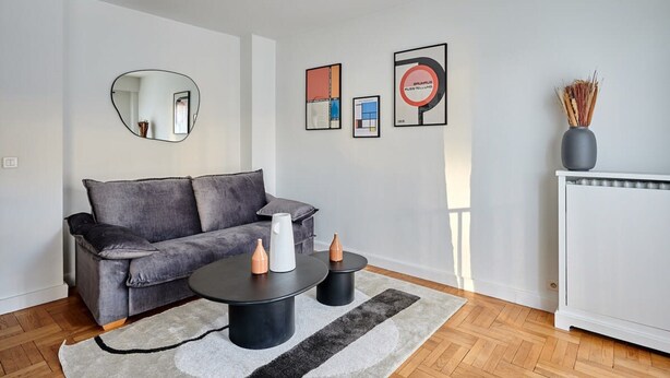 Ein modernes Wohnzimmer mit einem grauen Sofa, zwei schwarzen Couchtischen, einem weißen Heizkörper und gerahmten Kunstwerken an der Wand.