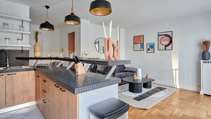 Moderni keittiö, jossa on keskeinen saareke, riippuvalaisimet sekä ruokailutila, jossa on sohva ja sohvapöytä.