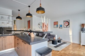 Eine moderne Küche mit Kochinsel, Pendelleuchten und einem Essbereich mit Sofa und Couchtisch.