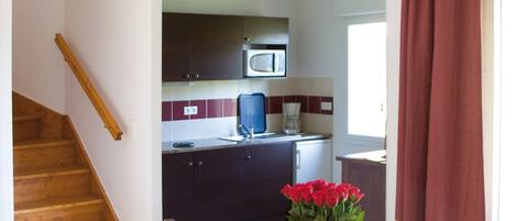 A kitchen with dark cabinets, a microwave, and a coffee maker. There's a dining table with chairs and a vase of flowers.