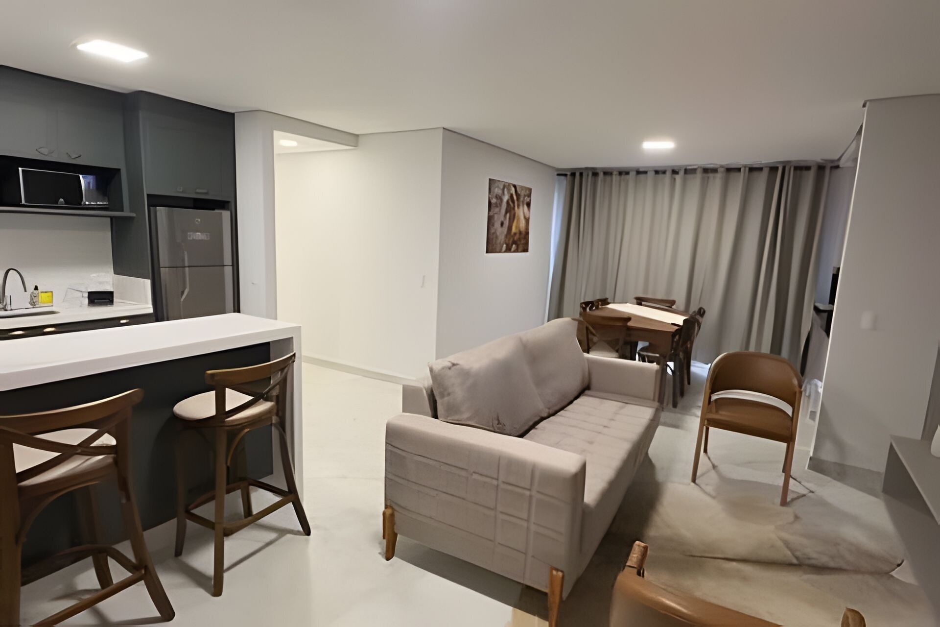 Et moderne køkken med hvid bordplade og barstole, en beige sofa, et spisebord med stole og et billede på væggen.