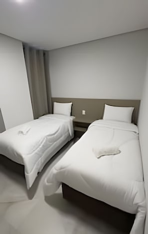 A hotel room with two single beds, a nightstand, a wall-mounted light, and a curtain. - Apartamento no centro de Foz do Iguaçu (Foz do Iguaçu)
