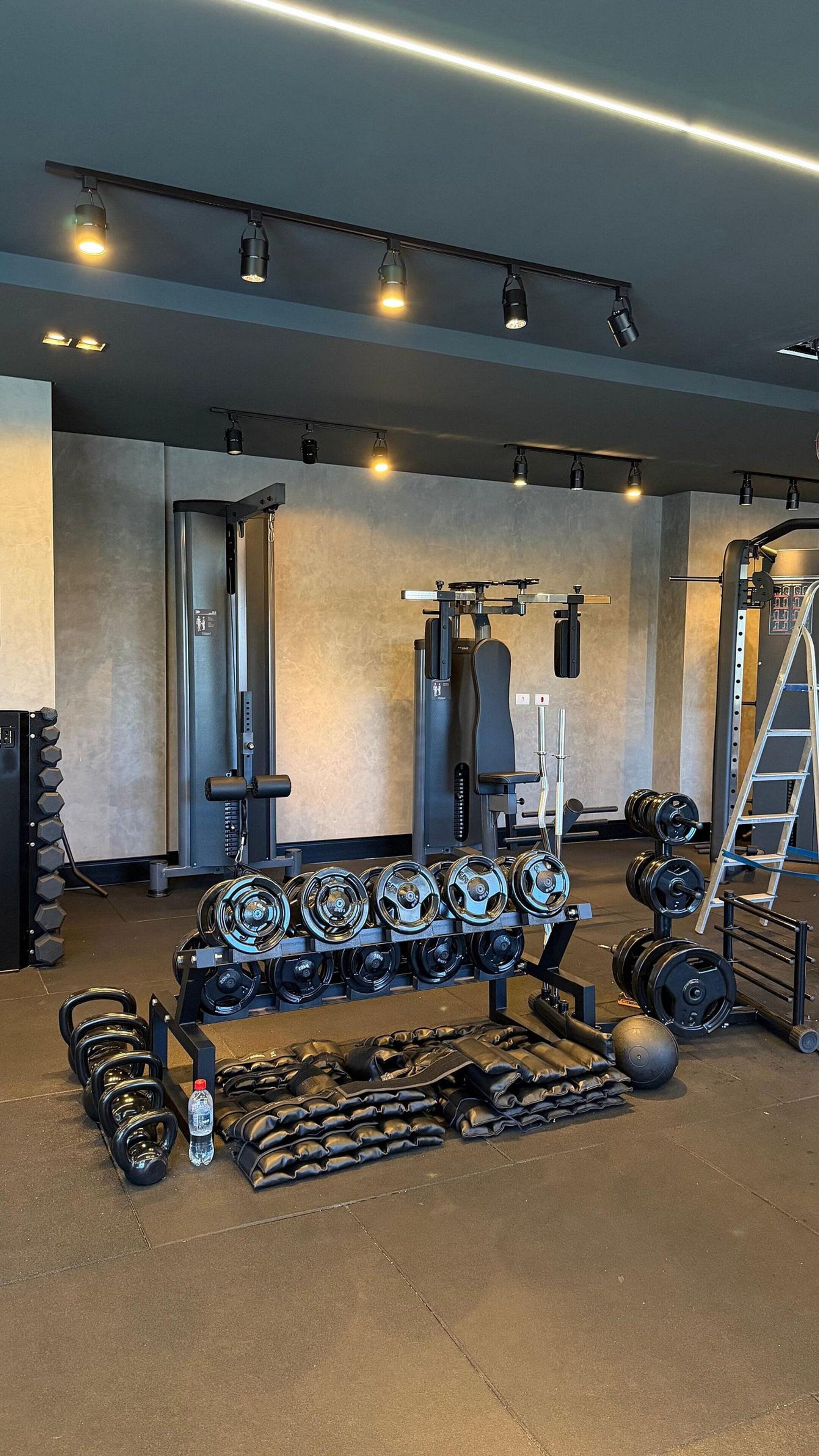 Uma academia com equipamentos de musculação, incluindo halteres, barras e uma estrutura para agachamento.