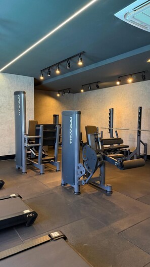A gym with various exercise equipment, including a treadmill, weight machines, and a wall-mounted fan. - Apartamento no centro de Foz do Iguaçu (Foz do Iguaçu)