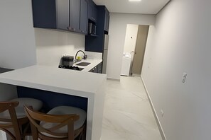 A compact kitchen with a white countertop, dark cabinets, and a small dining area with two wooden chairs. - Apartamento no centro de Foz do Iguaçu (Foz do Iguaçu)