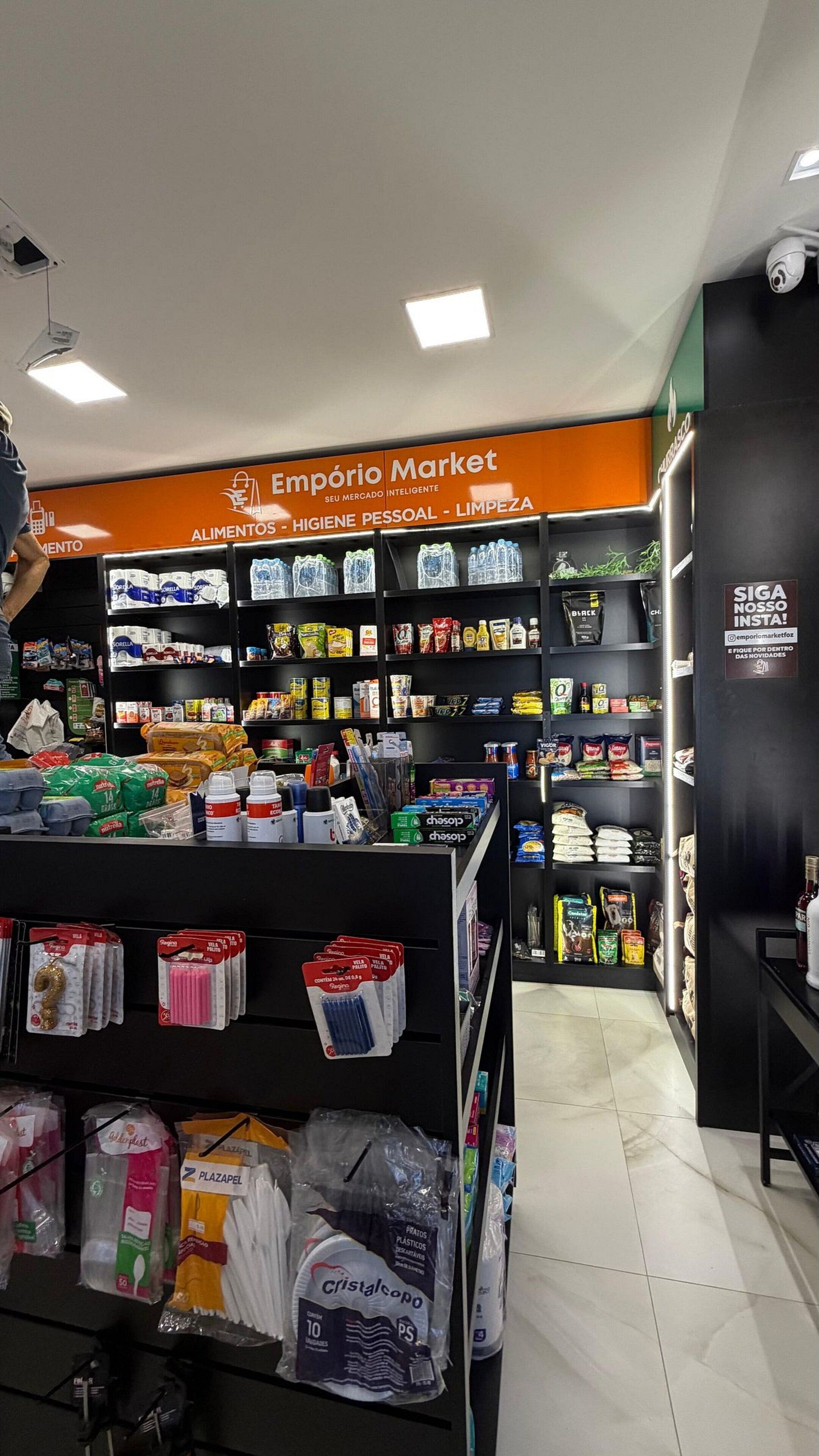 Interior de supermercado com prateleiras repletas de diversos produtos, incluindo alimentos e artigos para o lar.