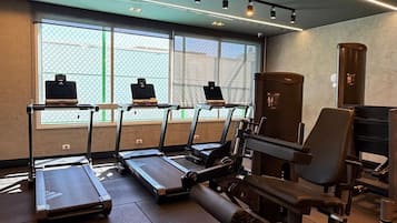 Et fitnessrum med løbebånd, romaskine og vægtbænk.