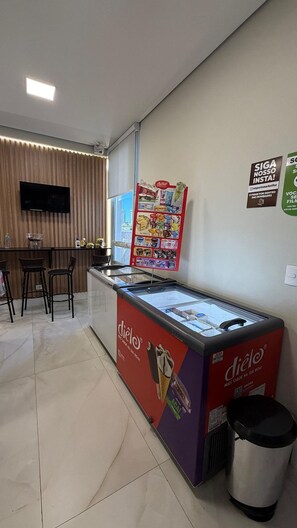 A small ice cream kiosk with a branded sign, a trash bin, and a seating area with chairs. - Apartamento no centro de Foz do Iguaçu (Foz do Iguaçu)