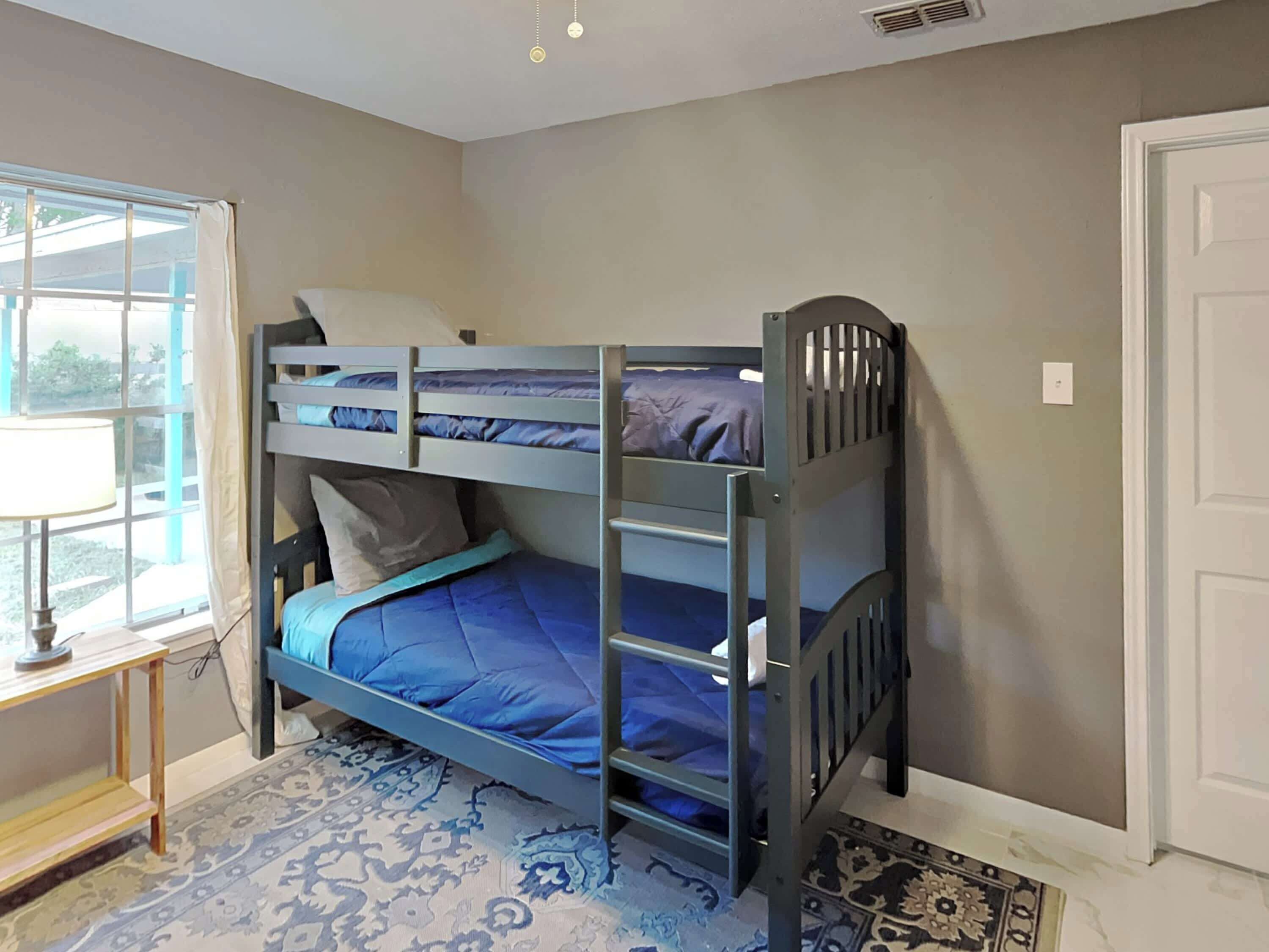 A bunk bed room with a window, a small table, and patterned carpet.