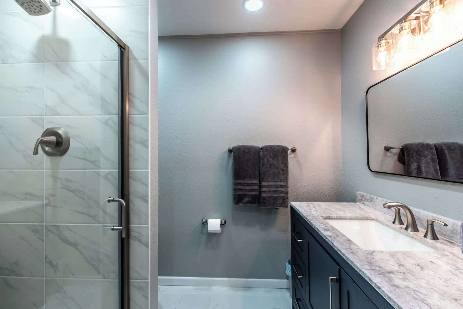 Un baño moderno con cabina de ducha de vidrio, encimera de mármol y un espejo grande.