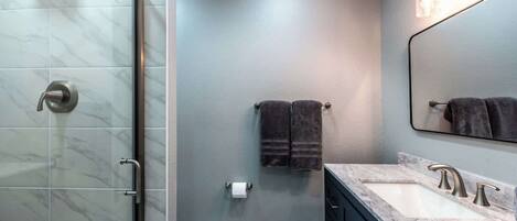 Un baño moderno con cabina de ducha de vidrio, encimera de mármol y un espejo grande.