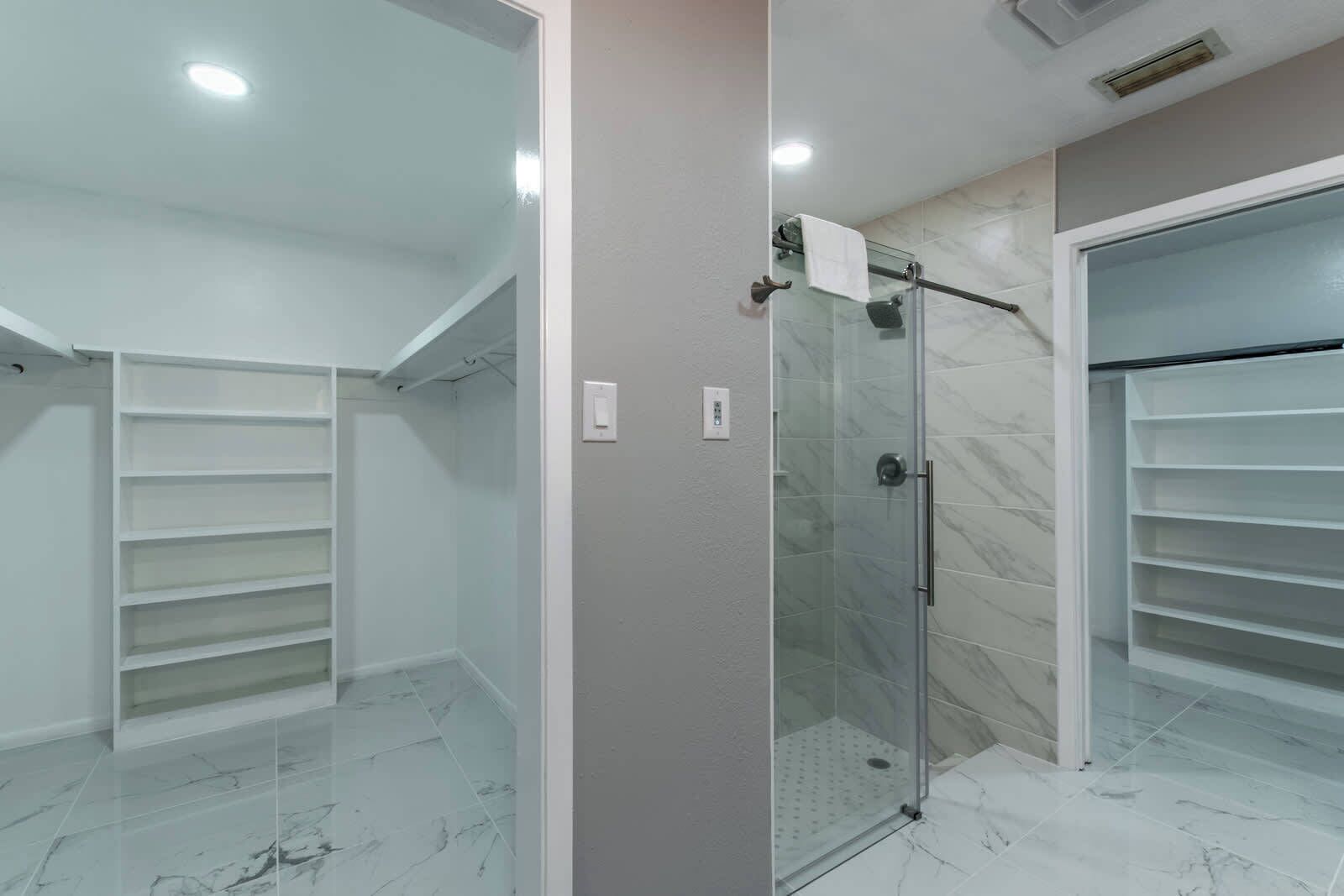 A modern bathroom with a glass shower enclosure, marble flooring, and built-in shelving.