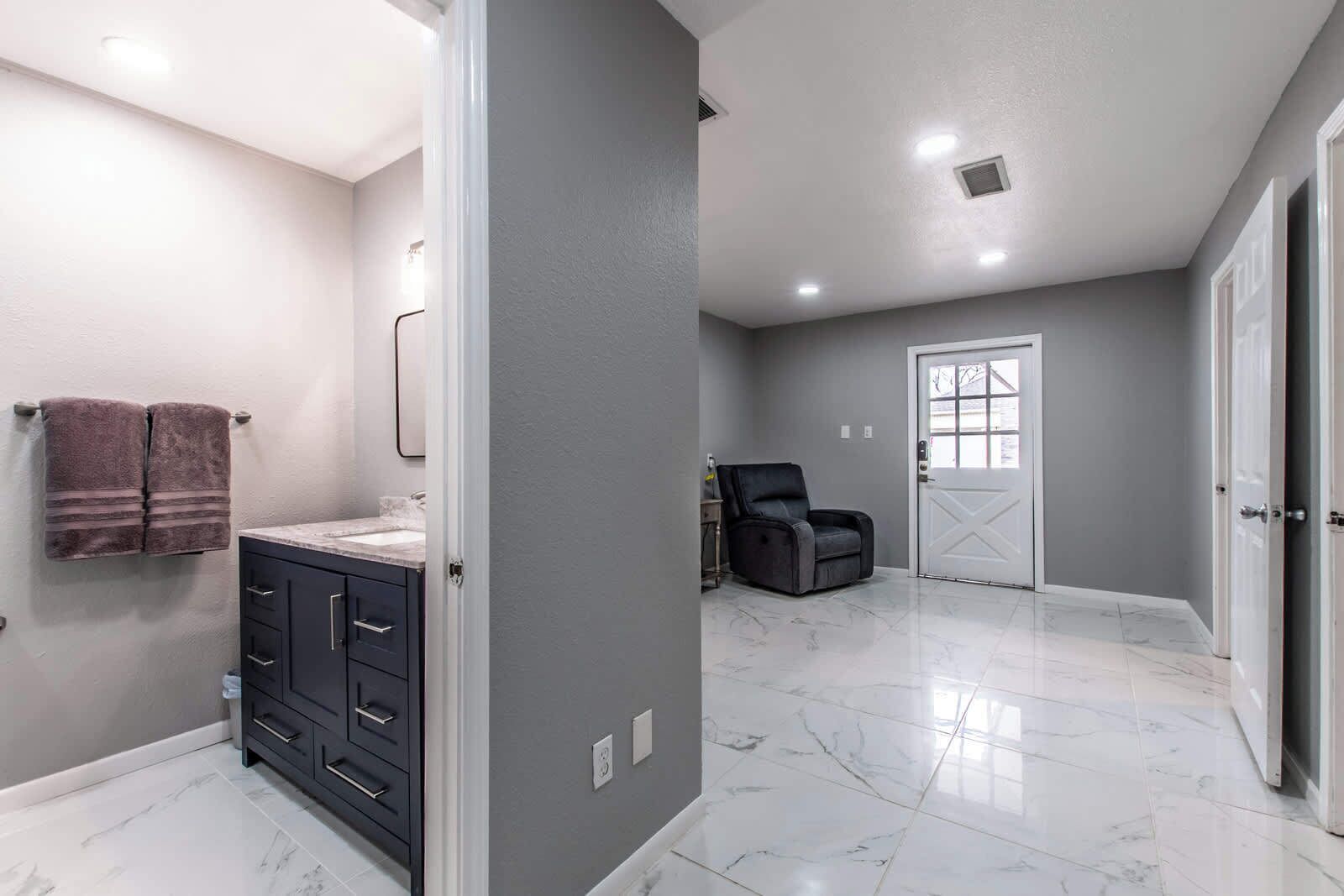 Um quarto amplo com piso de mármore, um sofá de cor escura e uma porta que dá para outro cômodo.