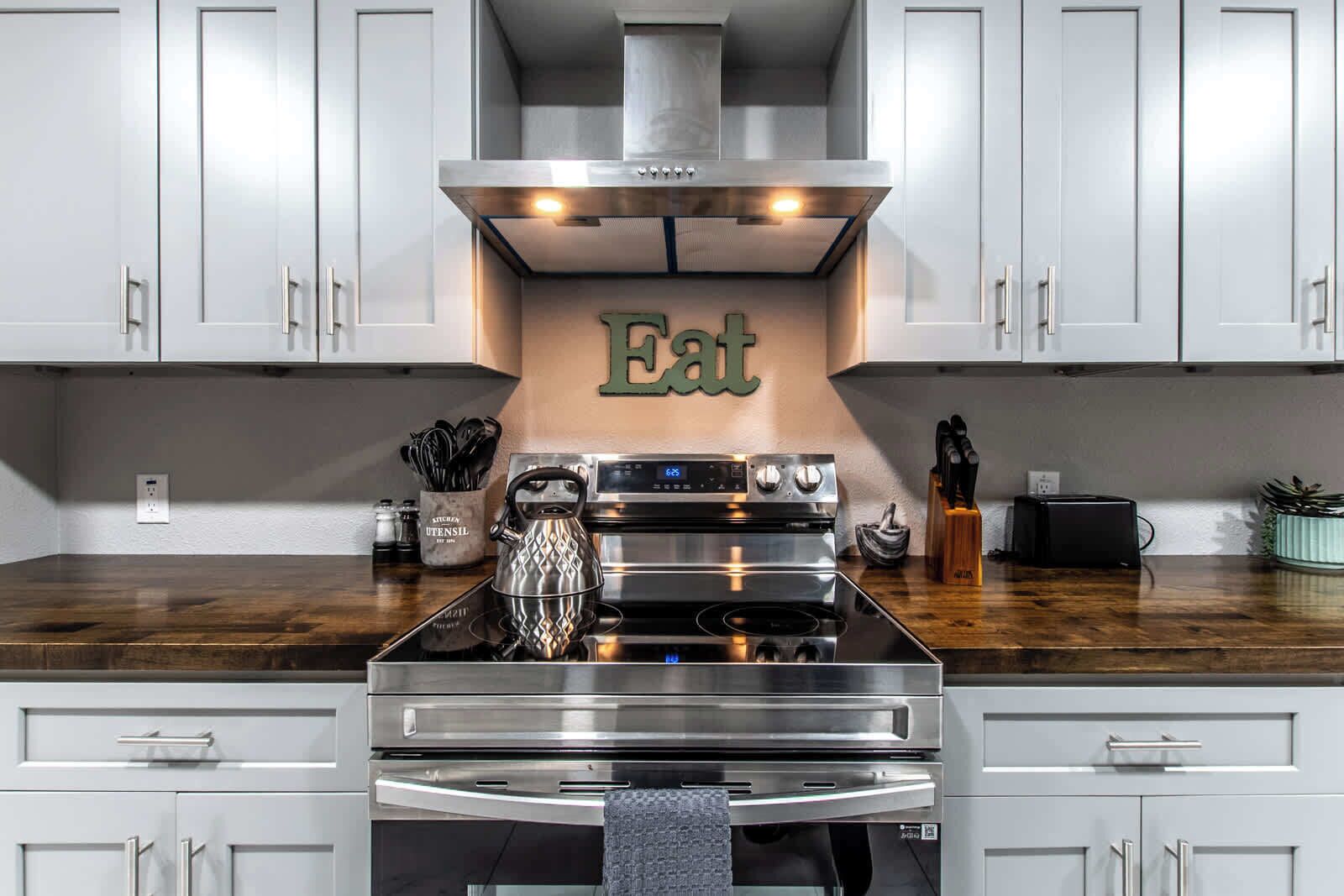 Una cocina moderna con electrodomésticos de acero inoxidable, encimera de madera y un letrero en la pared que dice 'Eat'.