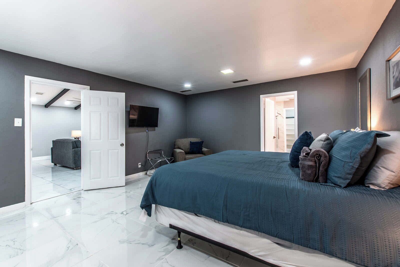 Un dormitorio con cama, televisor, puerta que da a otra habitación y baño a la vista por una puerta abierta.
