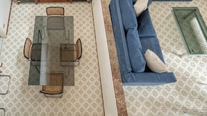 Una sala de estar con un sofá, una mesa de comedor con sillas, un aparador de madera y baldosas de suelo con diseños.