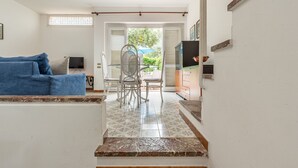Un pasillo que conduce a un comedor con una mesa y sillas, un sofá azul, un televisor y una escalera.
