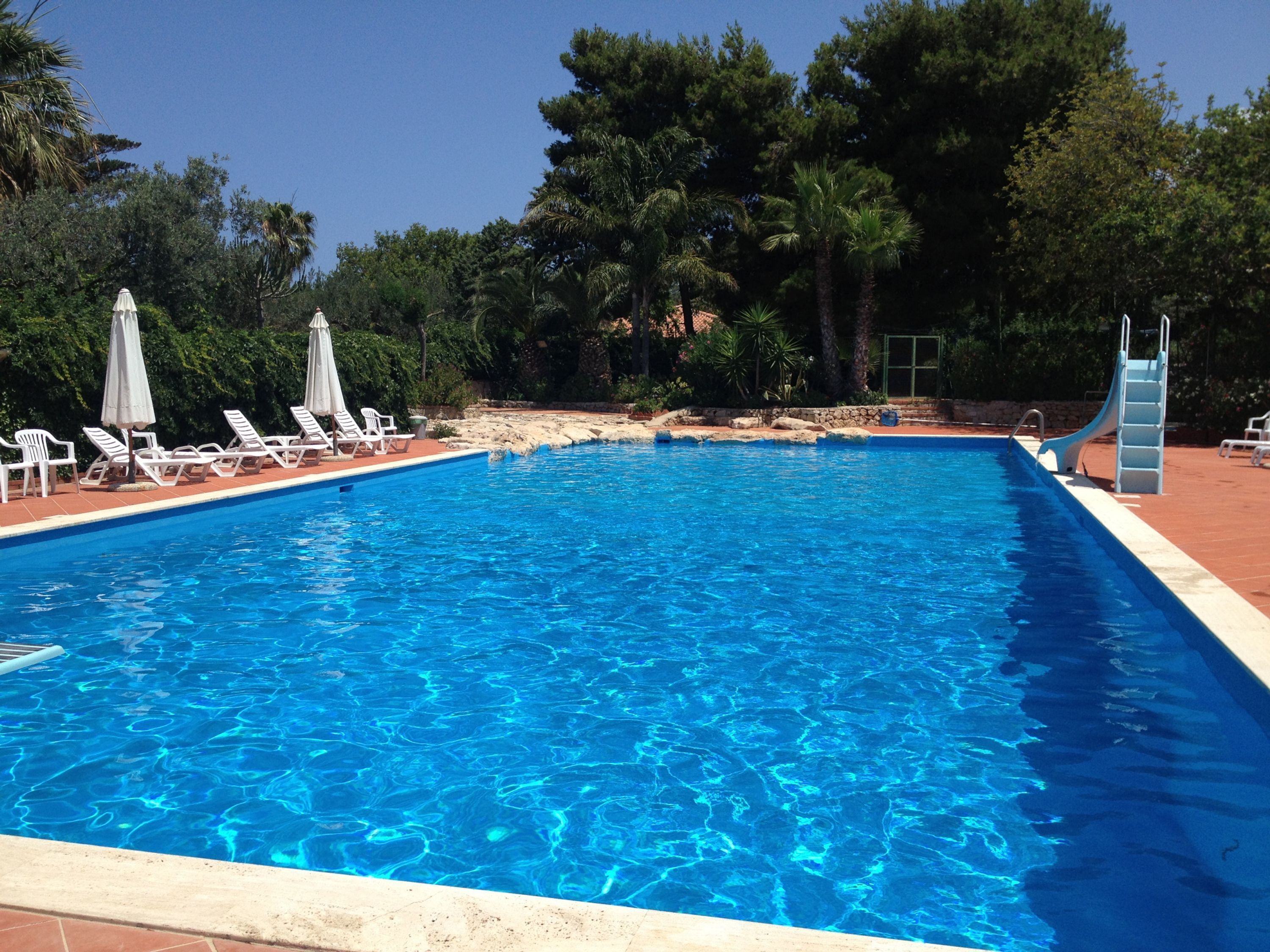 A swimming pool with clear blue water, surrounded by lounge chairs and umbrellas.
