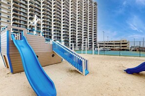 Ein Hochhaus mit einer Spielzone, darunter eine blaue Rutsche und eine kleine Holzkonstruktion.